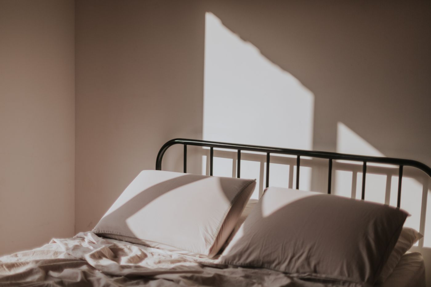 cama com travesseiros junto à parede, iluminada pela luz da manhã que entra pela janela