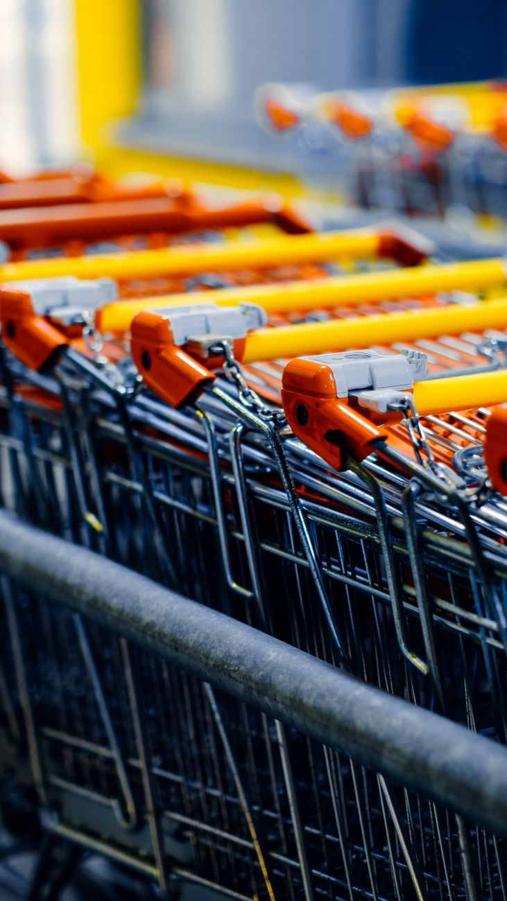 Carrinhos de compras vermelhos e amarelos enfileirados na entrada de um comércio