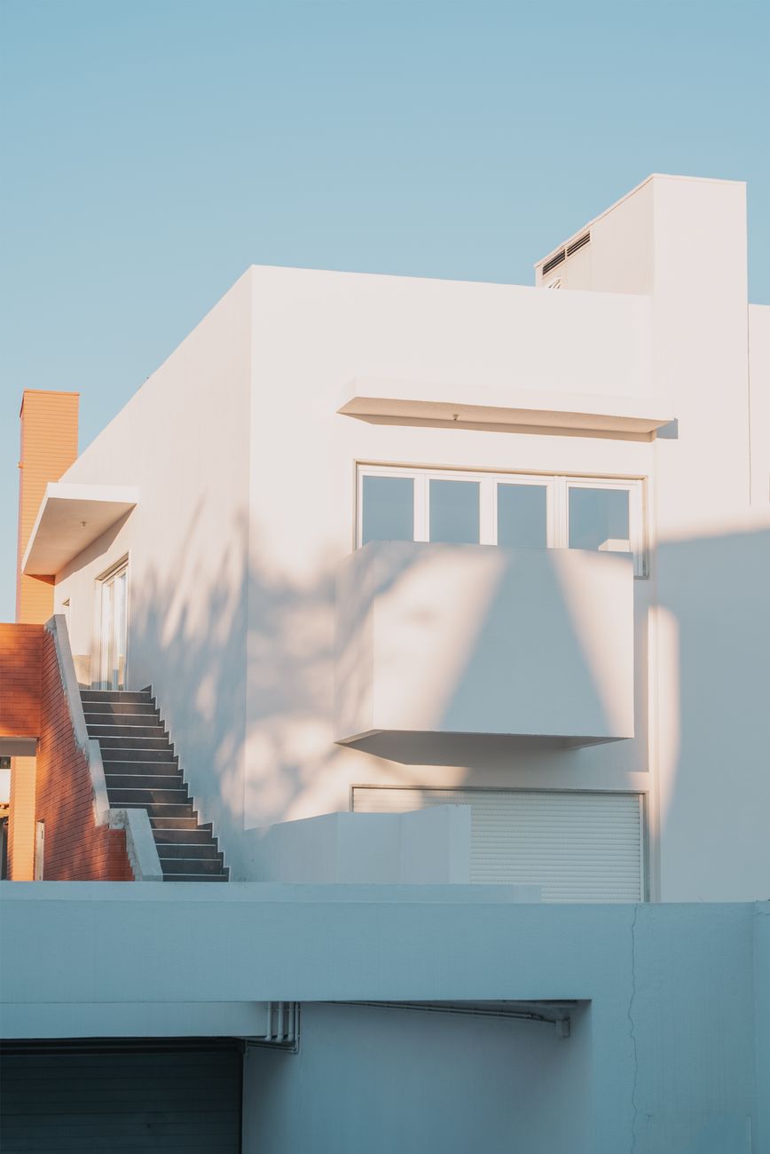 Fachada de casa moderna branca, com volumes que avançam e recuam formando recortes na construção