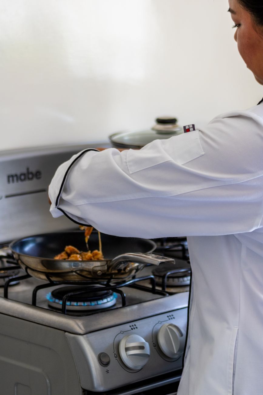 Pessoa cozinhando numa frigideira sobre o fogão, de frente para a parede da cozinha