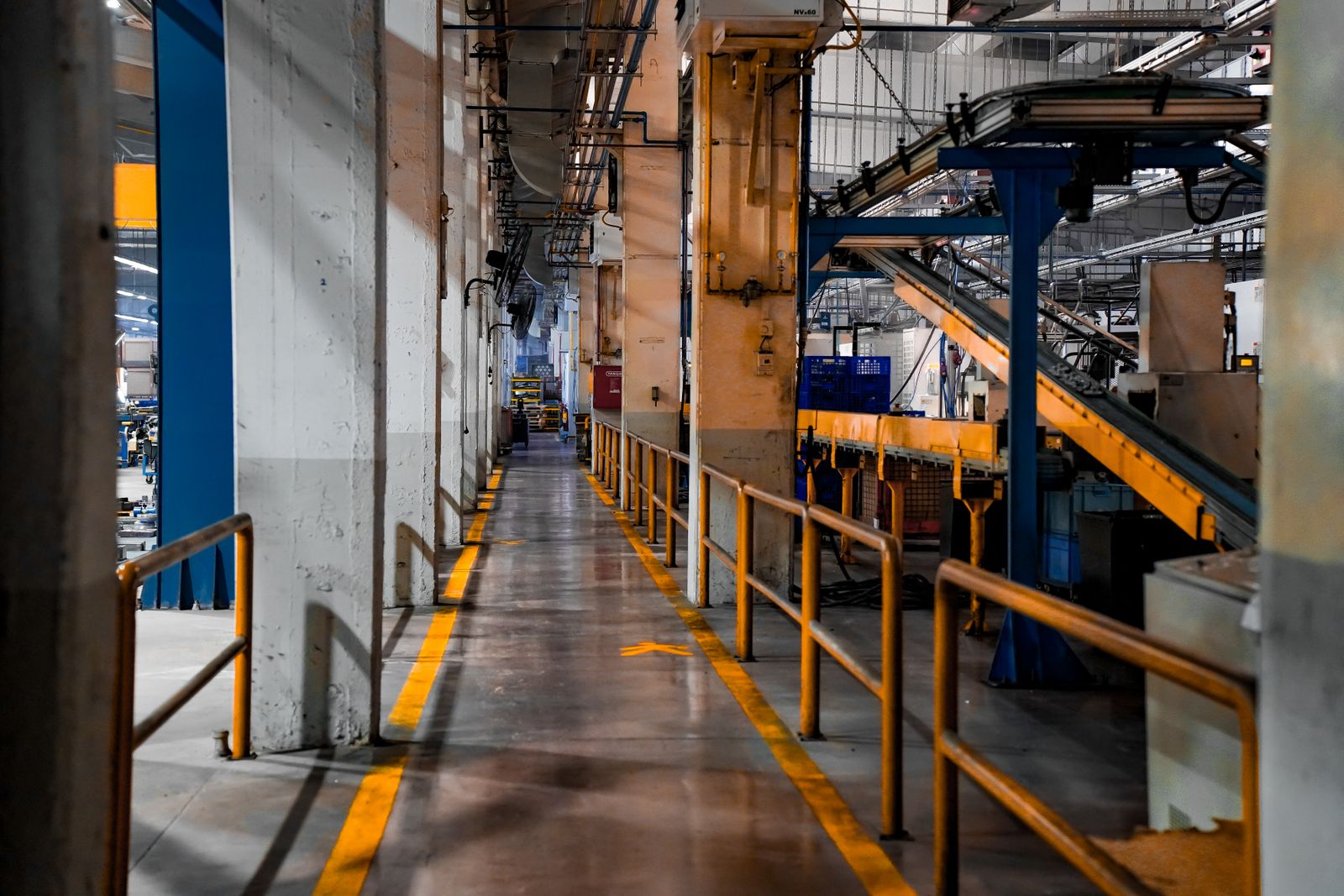 Corredor interno de uma fábrica, com linha de produção, esteira, maquinário e tubulação aparente no teto