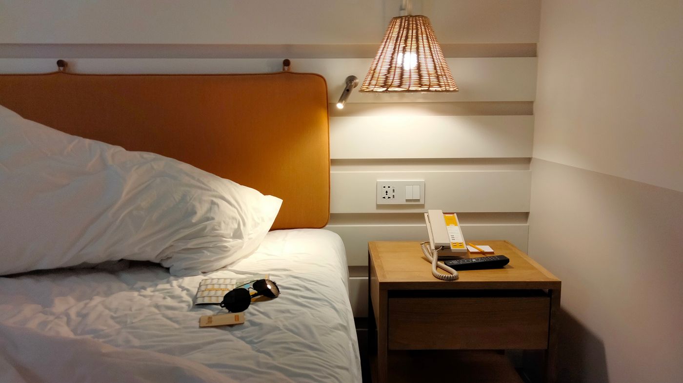 quarto à noite com mesa de cabeceira, telefone e tomada instalada na altura da cabeceira