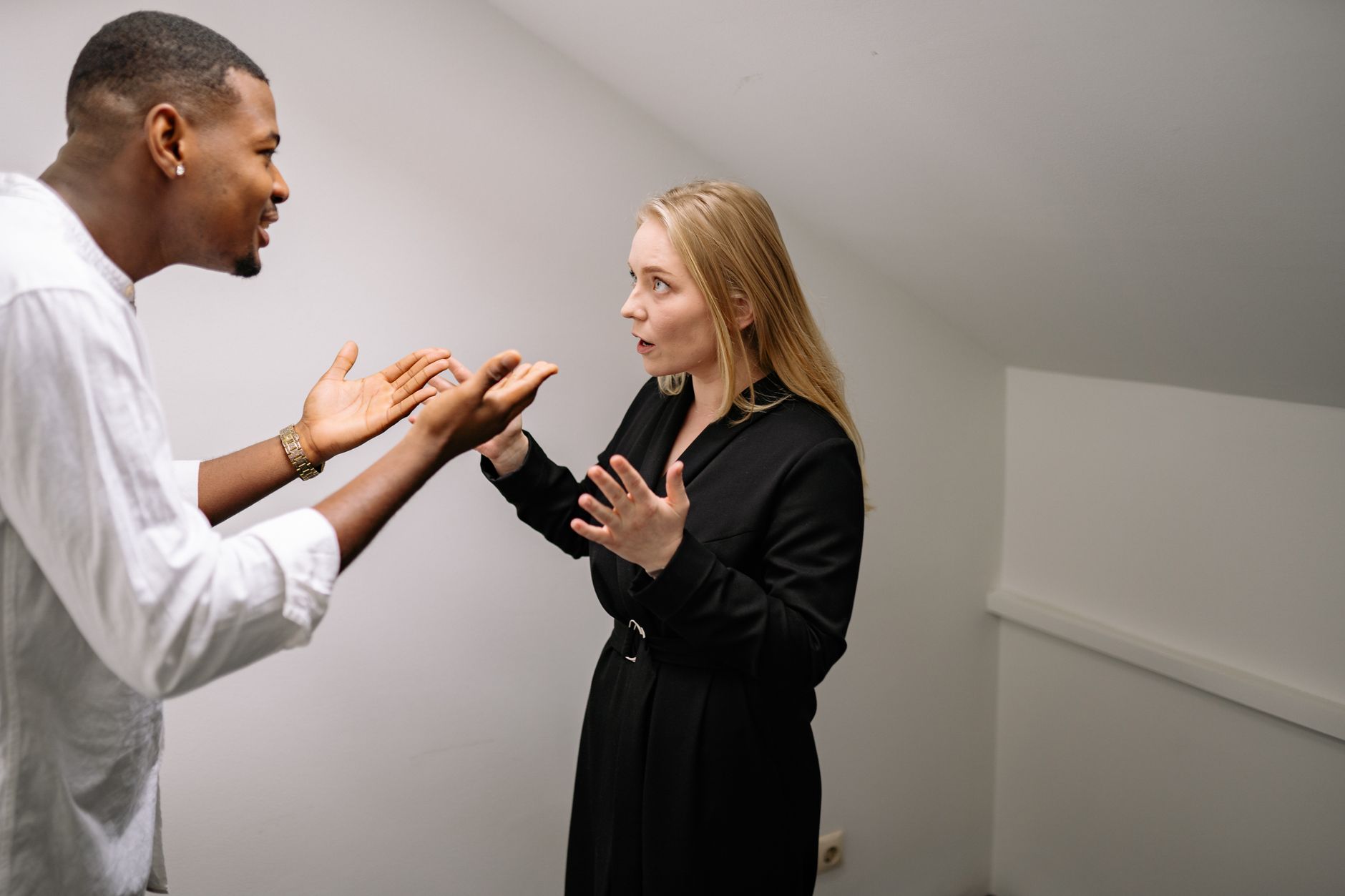 Dois adultos em roupa social discutindo em pé, frente a frente, num ambiente de trabalho