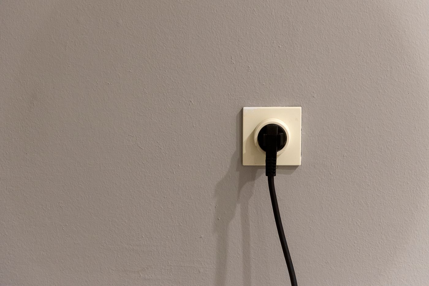 tomada de parede com um plugue preto conectado, em parede clara