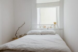 Cama de casal com a cabeceira embaixo da janela, num quarto branco
