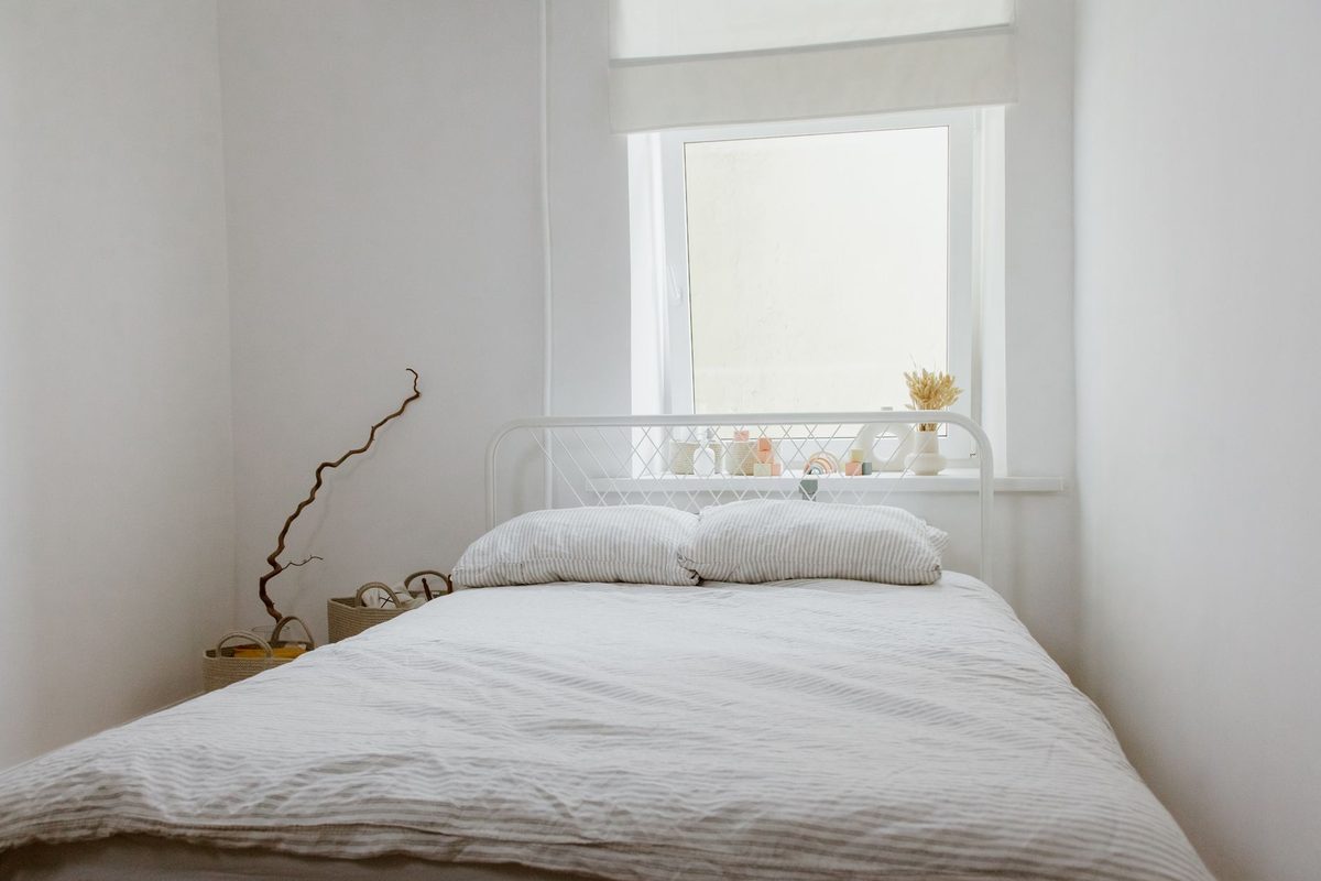 Cama de casal com a cabeceira embaixo da janela, num quarto branco