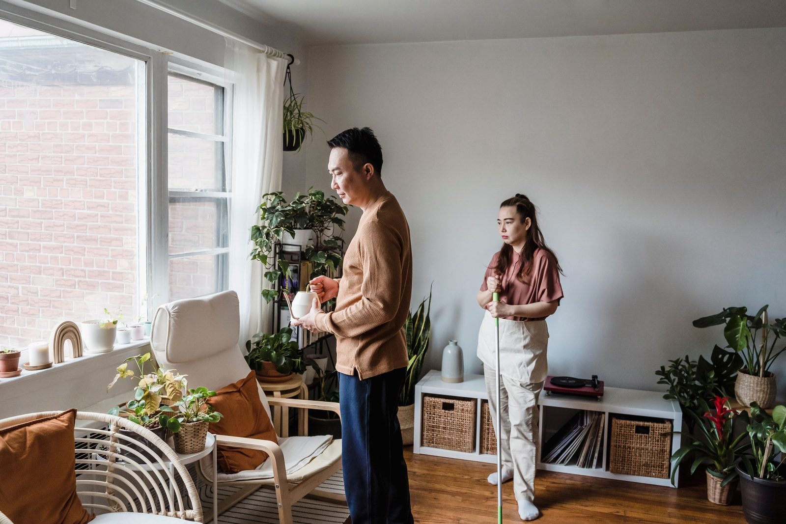 Casal em pé na sala de casa, entre plantas, conversando
