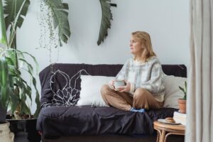 Mulher sentada no sofá da sala de casa, com uma xícara na mão, olhando o ambiente