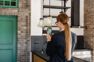 Mulher de costas fotografando a cozinha da própria casa com o celular