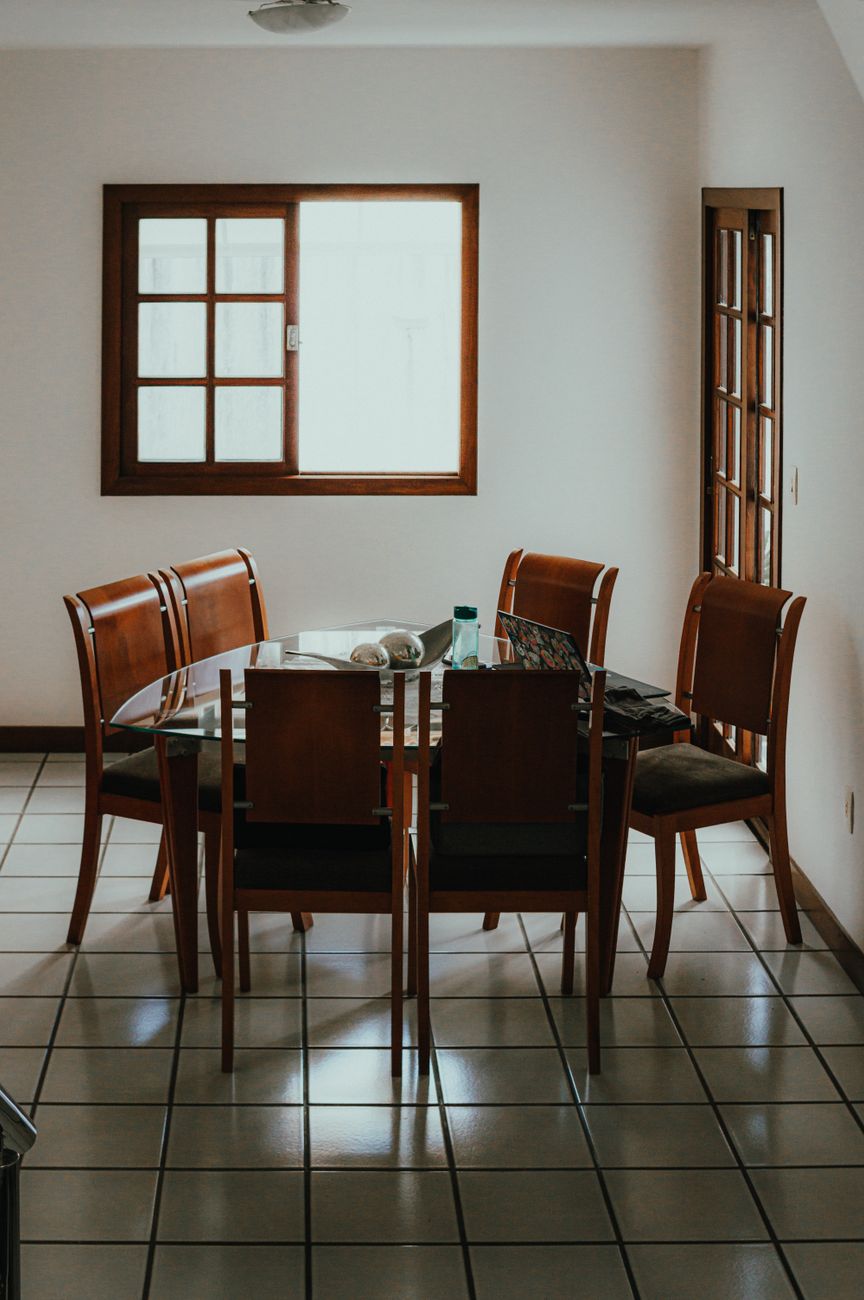 Mesa de jantar de vidro com cadeiras de madeira numa sala de casa brasileira
