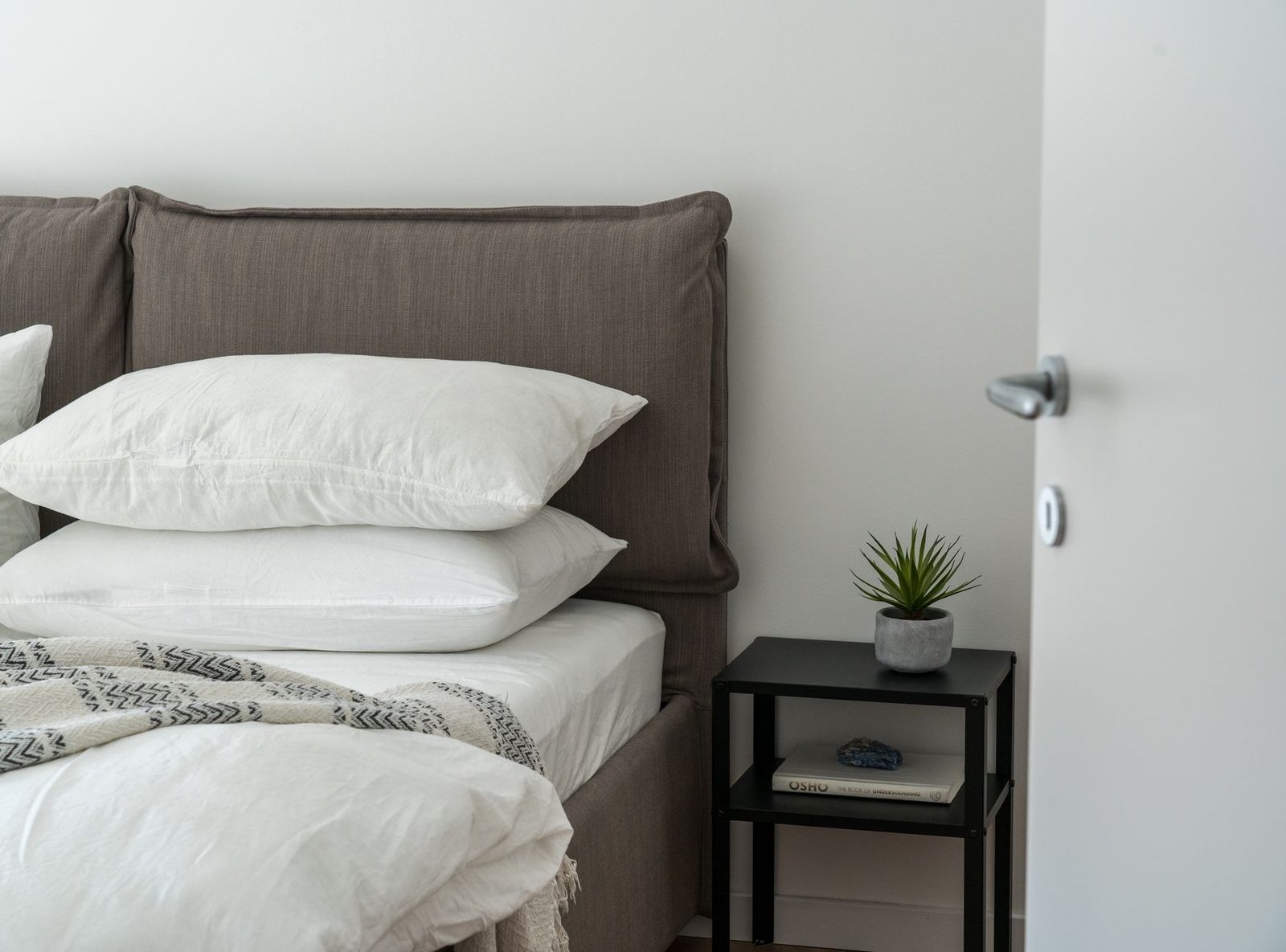 Cama de casal com cabeceira estofada e a porta do quarto logo ao lado