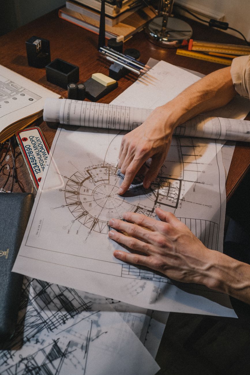 Mãos analisando a planta de um imóvel sobre a mesa, com lápis e régua ao lado